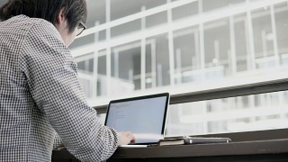 年轻的亚洲商人在工作空间使用笔记本电脑，木桌上放着智能手机和笔记本。男性用手在笔记本电脑键盘上打字。数字时代概念中的自由职业生活方式。视频素材模板下载
