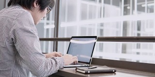 年轻的亚洲商人在工作空间的木桌上使用笔记本电脑和智能手机。男性用手在笔记本电脑键盘上打字。数字时代概念中的自由职业生活方式。