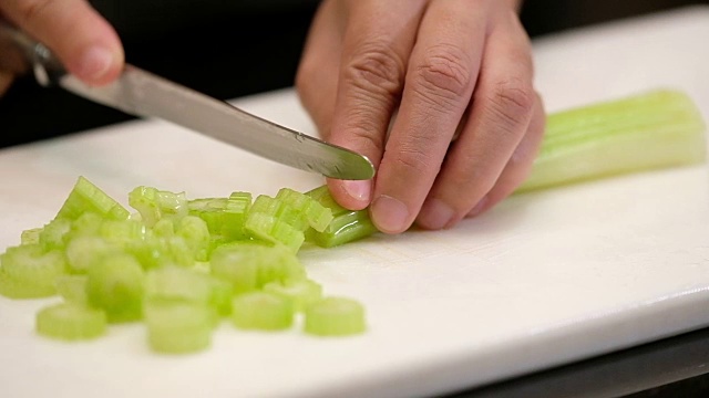 慢动作近手用刀将芹菜切在厨房的砧板上