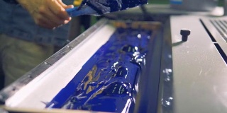 一个人在工厂印刷机的特殊装置上涂上厚厚的蓝色油漆。