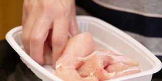 用手把生鸡肉放在厨房台面的塑料托盘里腌制