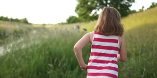 一个卷卷的女孩和她的狗在绿色的草丛中沿着小路跑。暑假，阖家欢乐渡假。那女孩穿着一件带有条纹的红衣服和一件白色连衣裙