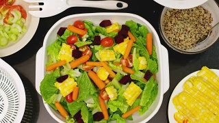 俯视图加速手拌新鲜蔬菜沙拉到厨房台面上的白色碗视频素材模板下载