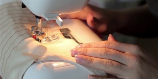 缝纫女工在缝纫机上剪布料并缝制的妇女。裁缝在机器上缝纫时用手托着布料。