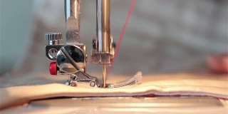 缝纫机关闭。缝牛仔宏。缝纫机的针慢动作缝着一块红色的厚布。线穿过织物。