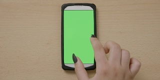 女人的手在绿色智能手机触摸屏上做缩放手势、滚动和滑动多媒体