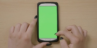 俯视图的少女手使用智能手机手势浏览社交媒体网络在绿色屏幕上
