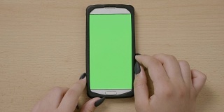 年轻女商人用智能手机在绿色触摸屏上做滚动和滑动手势的俯视图