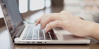 年轻的商人在工作空间的木桌上使用笔记本电脑和智能手机。男性用手在笔记本电脑键盘上打字。数字时代概念中的自由职业生活方式。