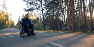 在森林里，一个瘫痪的人正靠他的电动轮椅沿着道路行走