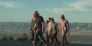 一群三十多岁的人一起徒步行走在科罗拉多大路口的科罗拉多国家纪念碑的沙漠里，俯瞰日落时分的书克利夫
