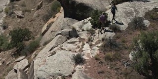 两个人在科罗拉多州大Junction沙漠的科罗拉多国家纪念碑的岩石边缘上行走的航拍照片