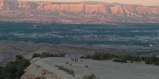 航拍的一组三十多岁的人一起徒步旅行在沙漠的科罗拉多国家纪念碑大汇合点，俯瞰日落的书悬崖科罗拉多州