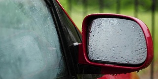 特写镜头，雨点在汽车的玻璃窗上滴落下来。雨点落在侧面的镜子上。有大雨，阵雨。雨滴落在汽车玻璃上