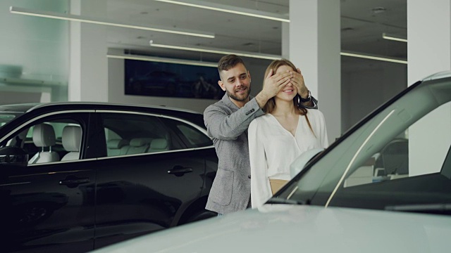 快乐的男人是让惊喜他的妻子闭上她的眼睛与他的手，并带领她到美丽的新车是汽车展厅，快乐的女人是拥抱和亲吻他。
