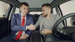 汽车经销商正在给愉快的男买家钥匙卡，男人们在试驾后坐在车内握手、微笑、交谈。购买交通和人的概念。视频素材模板下载