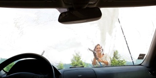 微笑的女性用高压清洗喷枪清洗她的汽车泡沫挡风玻璃