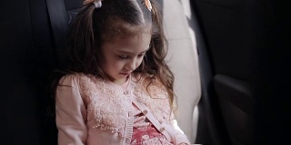 漂亮的蓝眼睛小女孩坐在后座上。她专注地玩手机游戏。