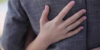 女性的手近距离抚摸抚摸着男人的背部，慢动作浅拍昂贵的衣服珠宝戒指。新娘抱着新郎的腰散焦自然背景。婚礼时尚爱情关系