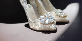 女性白色蕾丝设计鞋与闪亮的钻石站近室内在黑暗的背景文字。婚礼豪华鞋与宝石架焦点闪亮在地板上。新娘时装设计师