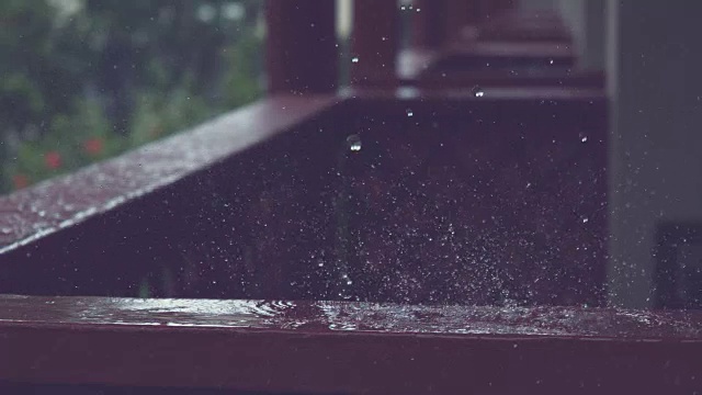 慢动作:小雨滴落在黑色的木栏杆上，溅过门廊。