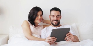 微笑的夫妇在床上与平板电脑