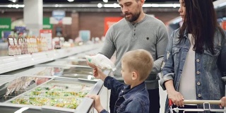 现代的家庭在超市购买预先煮好的冷冻食品，男孩打开冰箱拿袋子，他的父母在检查过期日期和配料内容。