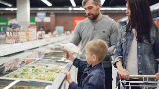 现代的家庭在超市购买预先煮好的冷冻食品，男孩打开冰箱拿袋子，他的父母在检查过期日期和配料内容。视频素材模板下载