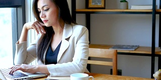 4K视频，忙碌的商务女性用笔记本电脑工作，严肃的思考在咖啡馆咖啡厅的早晨，商务人士的生活方式。30多岁的亚洲模特