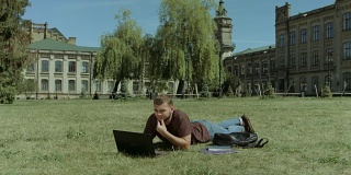 聪明的男学生在校园草坪上用笔记本电脑工作