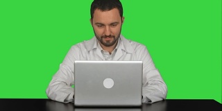 微笑的男医生坐在桌子上，笔记本电脑在绿色屏幕上，Chroma Key