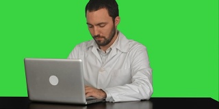 年轻的医生思考的想法与笔记本电脑在桌子上的绿色屏幕，色度键
