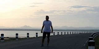 男人用智能手机听音乐和跑步的时间在日出的大坝公路上锻炼。健康生活理念。