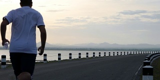 一名男子在日出的时候在大坝公路上慢跑锻炼。健康生活理念。起床跑步