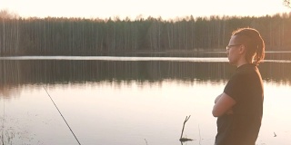 池塘上的渔夫。一个戴眼镜的年轻人穿着t恤钓鱼竿。