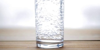 水从瓶子倒进木桌上的玻璃杯里