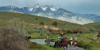 在诗情画意的犹他谷，牛仔和女牛仔骑马穿过河流