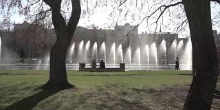 城市的喷泉。镜头。人们在公园里散步。喷泉在城市公园在炎热的夏天。在美丽的城市喷泉中，水流，水滴和明亮的水花