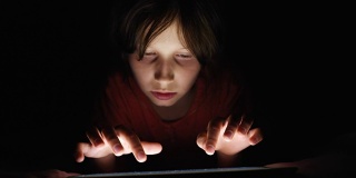多莉拍摄的白人女孩躺在床上玩平板电脑在黑暗的光下在互联网上。