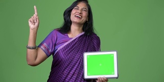 成熟快乐美丽的印度女人一边思考一边展示平板电脑，手指向上