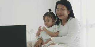 一位泰国母亲带着她的宝贝女儿在她的房间里用笔记本电脑看卡通片