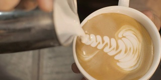 咖啡师把牛奶倒进热咖啡里，在咖啡馆里画叶子