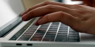 近距离的手打字键盘电脑笔记本在办公室。一个年轻女子只使用台式电脑。
