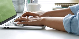 近距离的手打字键盘电脑笔记本在办公室。一个年轻女子只使用台式电脑。