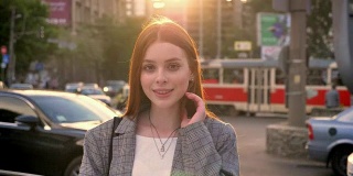 年轻姜女子的肖像在镜头和站在城市街道在日落，微笑，车辆的背景