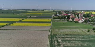 鸟瞰图风力涡轮机和农田在一个春日附近的村庄在慢镜头
