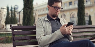 一名深色皮肤的男子正在公园里用智能手机收发短信