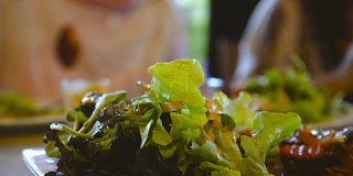 近距离拍摄一盘新鲜的绿色沙拉，而亚洲老妇人倒酱和吃素食在餐厅。健康饮食与饮食观念。