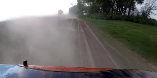 尘土从车轮升起，汽车行驶在农村的砾石路上。