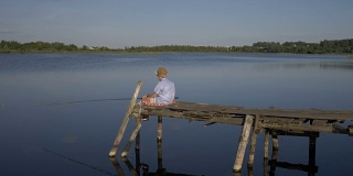 男孩坐在码头上，在湖里钓鱼，想着一些事情